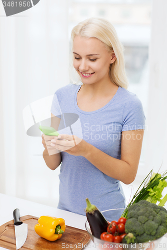 Image of smiling woman with smartphone cooking vegetables