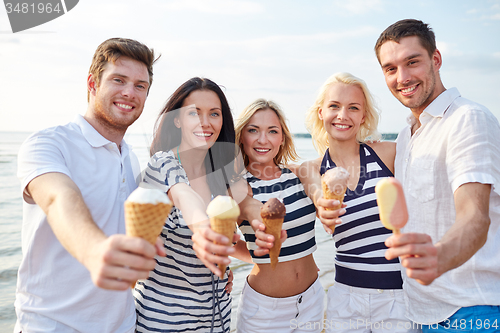Image of smiling friends eating ice cream on beach