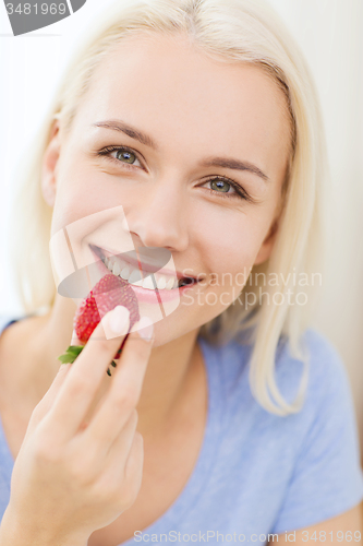 Image of happy woman eating strawberry at home