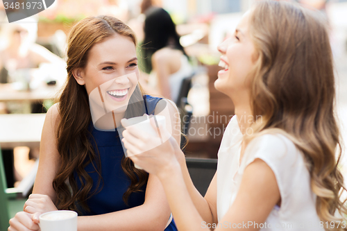 Image of smiling young women with coffee cups at cafe