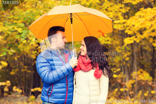 Image of smiling couple with umbrella in autumn park