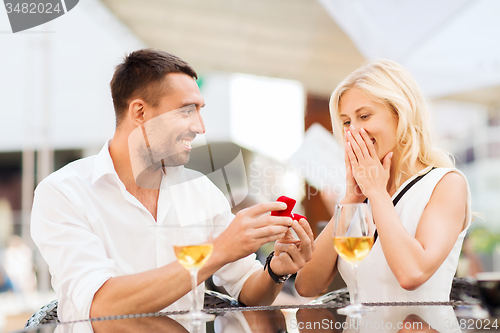 Image of happy couple with engagement ring and wine at cafe