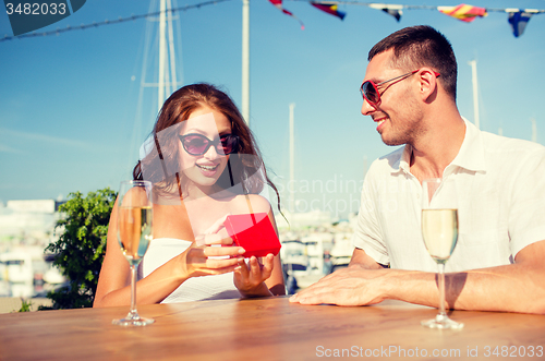 Image of smiling couple with champagne and gift at cafe