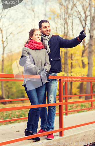 Image of smiling couple hugging on bridge in autumn park