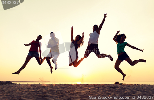 Image of smiling friends dancing and jumping on beach