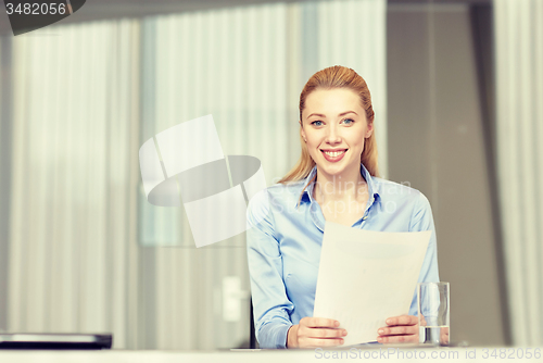 Image of smiling woman holding papers in office