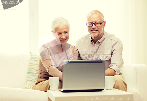 Image of happy senior couple with laptop and cups at home