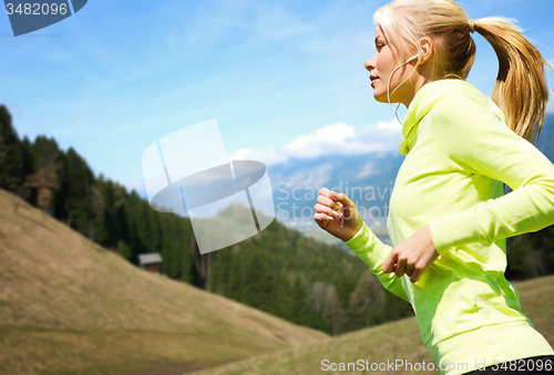 Image of happy young woman with earphones jogging outdoors