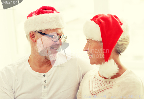 Image of happy senior couple in santa helper hats at home