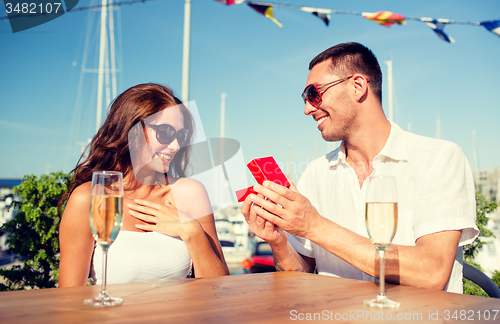 Image of smiling couple with champagne and gift at cafe