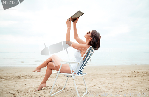 Image of happy woman with tablet pc taking selfie on beach