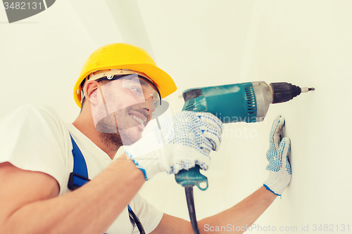 Image of smiling builder in hardhat drilling wall indoors