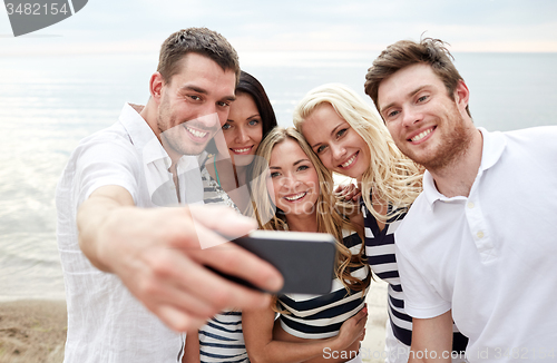 Image of happy friends on beach and taking selfie