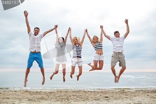 Image of smiling friends in sunglasses walking on beach