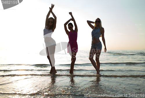 Image of happy female friends dancing on beach