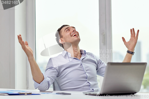 Image of happy businessman with laptop in office