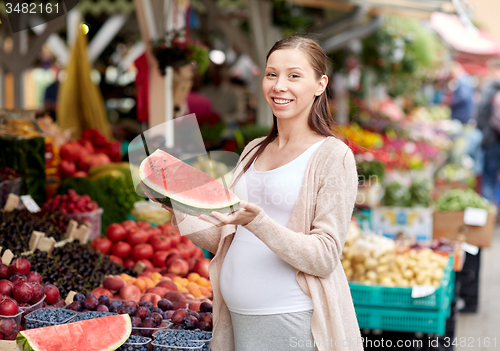 Image of pregnant woman holding watermelon at street market