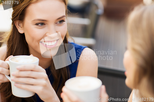 Image of smiling young women with coffee cups at cafe