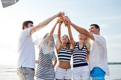 Image of smiling friends clinking bottles on beach