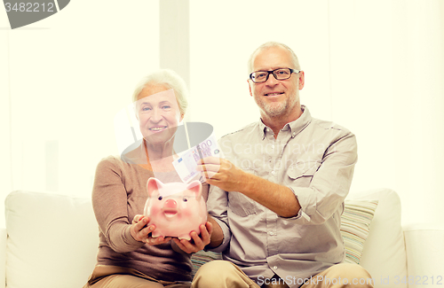 Image of senior couple with money and piggy bank at home