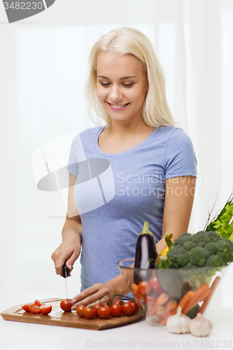 Image of smiling young woman chopping vegetables at home