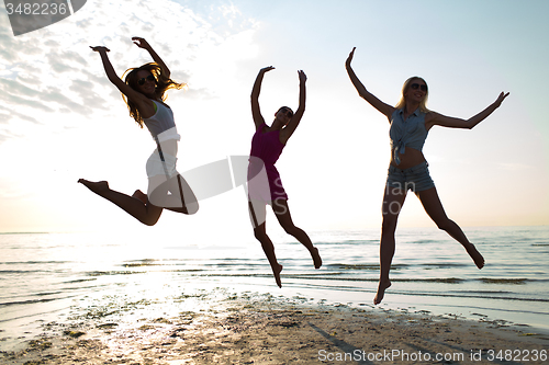 Image of happy female friends dancing and jumping on beach