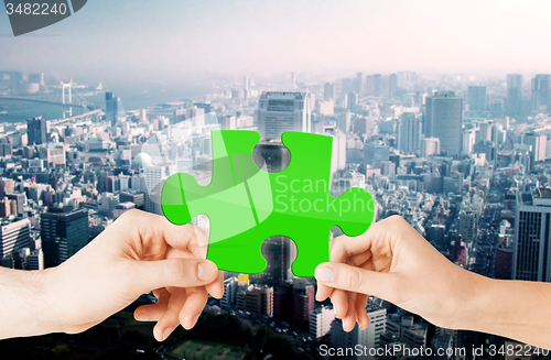 Image of hands with green puzzle over city background