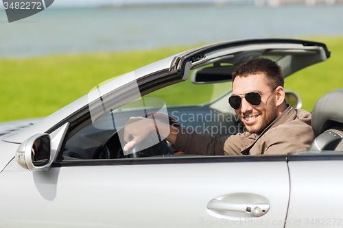 Image of happy man driving cabriolet car outdoors