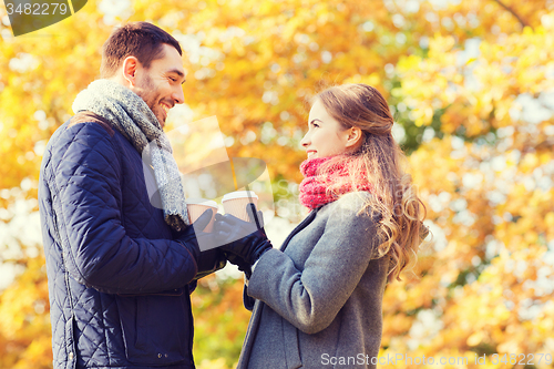 Image of smiling couple with coffee cups in autumn park