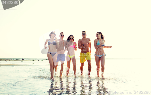 Image of smiling friends in sunglasses running on beach