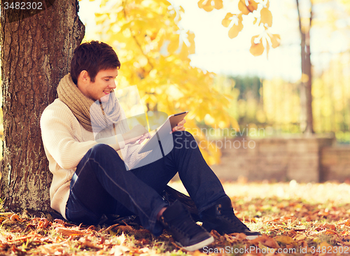 Image of smiling young man with tablet pc in autumn park