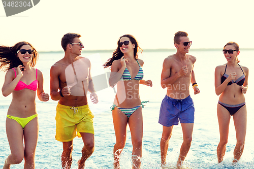 Image of smiling friends in sunglasses running on beach