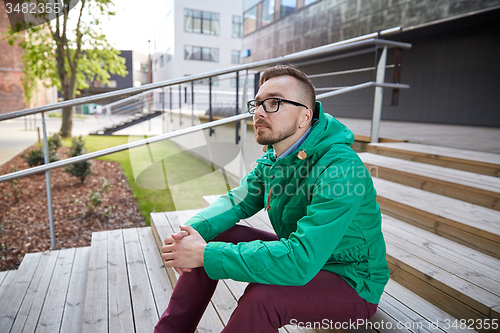 Image of happy young hipster man sitting on stairs in city