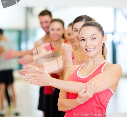 Image of group of smiling people stretching in the gym