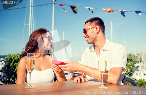 Image of smiling couple with champagne and gift at cafe