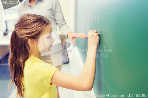 Image of little smiling schoolgirl writing on chalk board