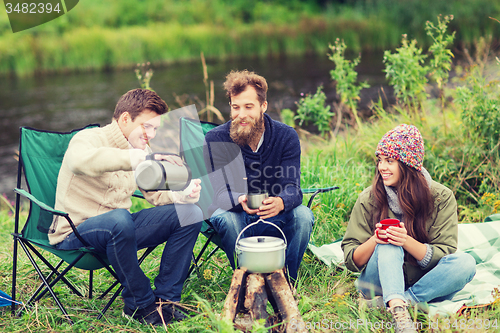 Image of group of smiling tourists cooking food in camping