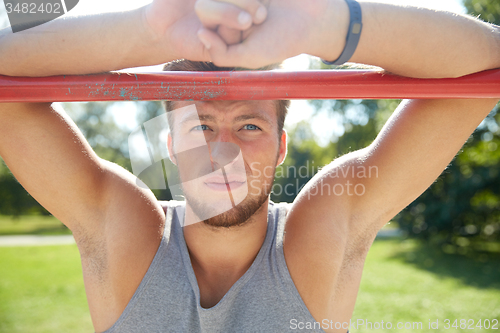 Image of young man exercising on horizontal bar outdoors