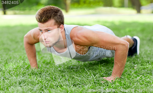 Image of young man doing push ups on grass in summer park