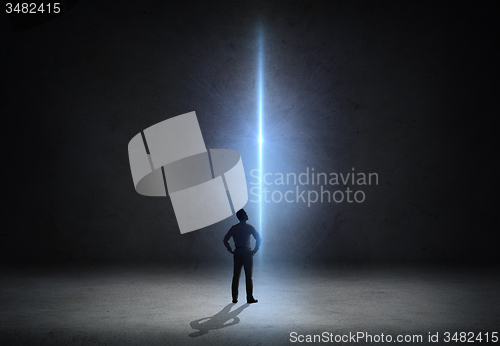 Image of businessman looking at ray of light over dark room