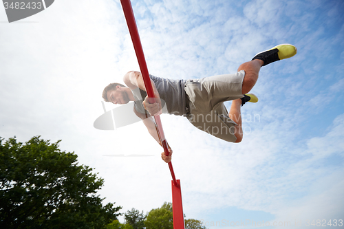 Image of young man exercising on horizontal bar outdoors