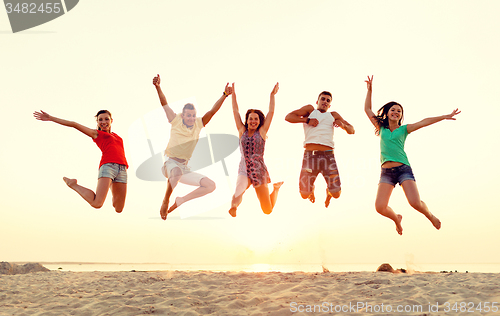 Image of smiling friends dancing and jumping on beach