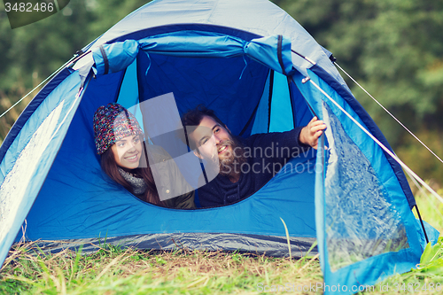 Image of smiling couple of tourists looking out from tent