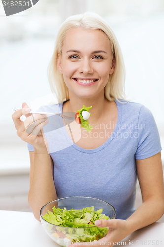 Image of smiling young woman eating salad at home