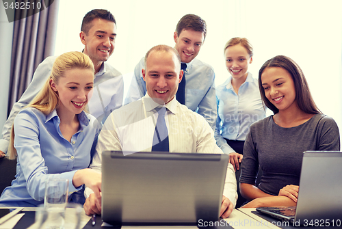 Image of smiling business people with laptop in office