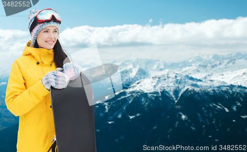 Image of happy young woman with snowboard over mountains