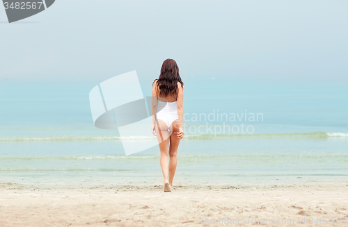 Image of young woman in swimsuit walking on beach