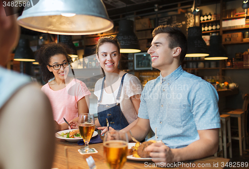 Image of happy friends eating and drinking at bar or pub