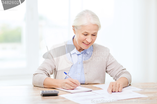 Image of senior woman with papers and calculator at home