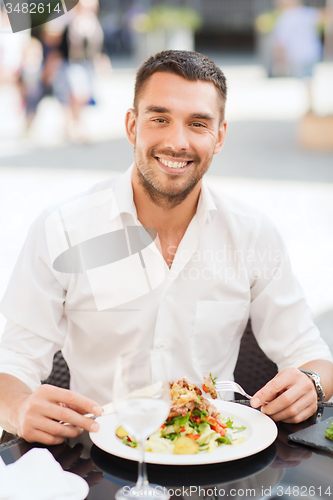 Image of happy man eating salad for dinner at restaurant